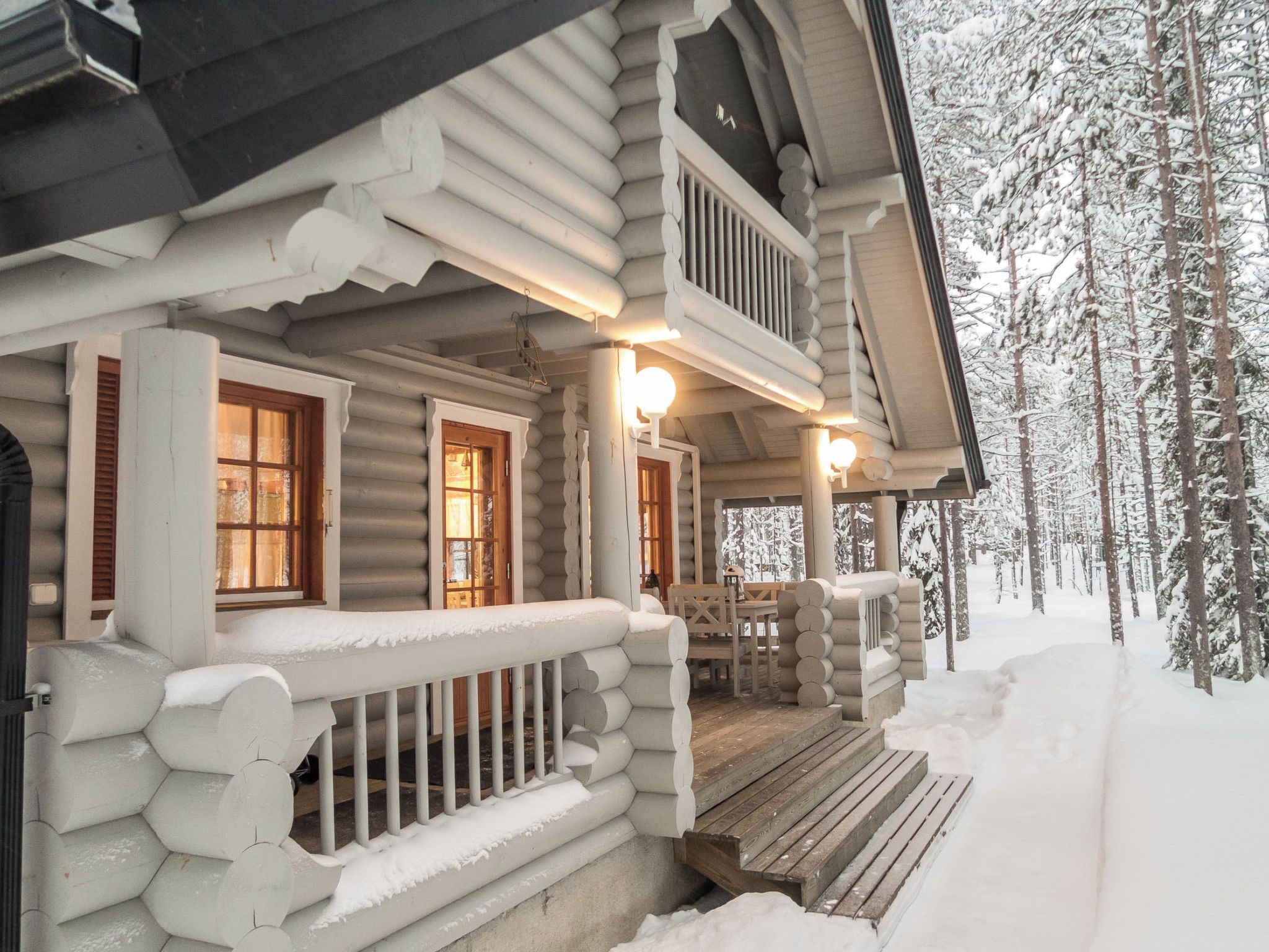 A log cabin with a porch, wooden shutters, and a snow-covered landscape.