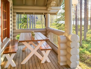 A wooden deck with a picnic table and benches, surrounded by a white railing and a view of a forest. - Syväniemi by Interhome (Kuusamo)