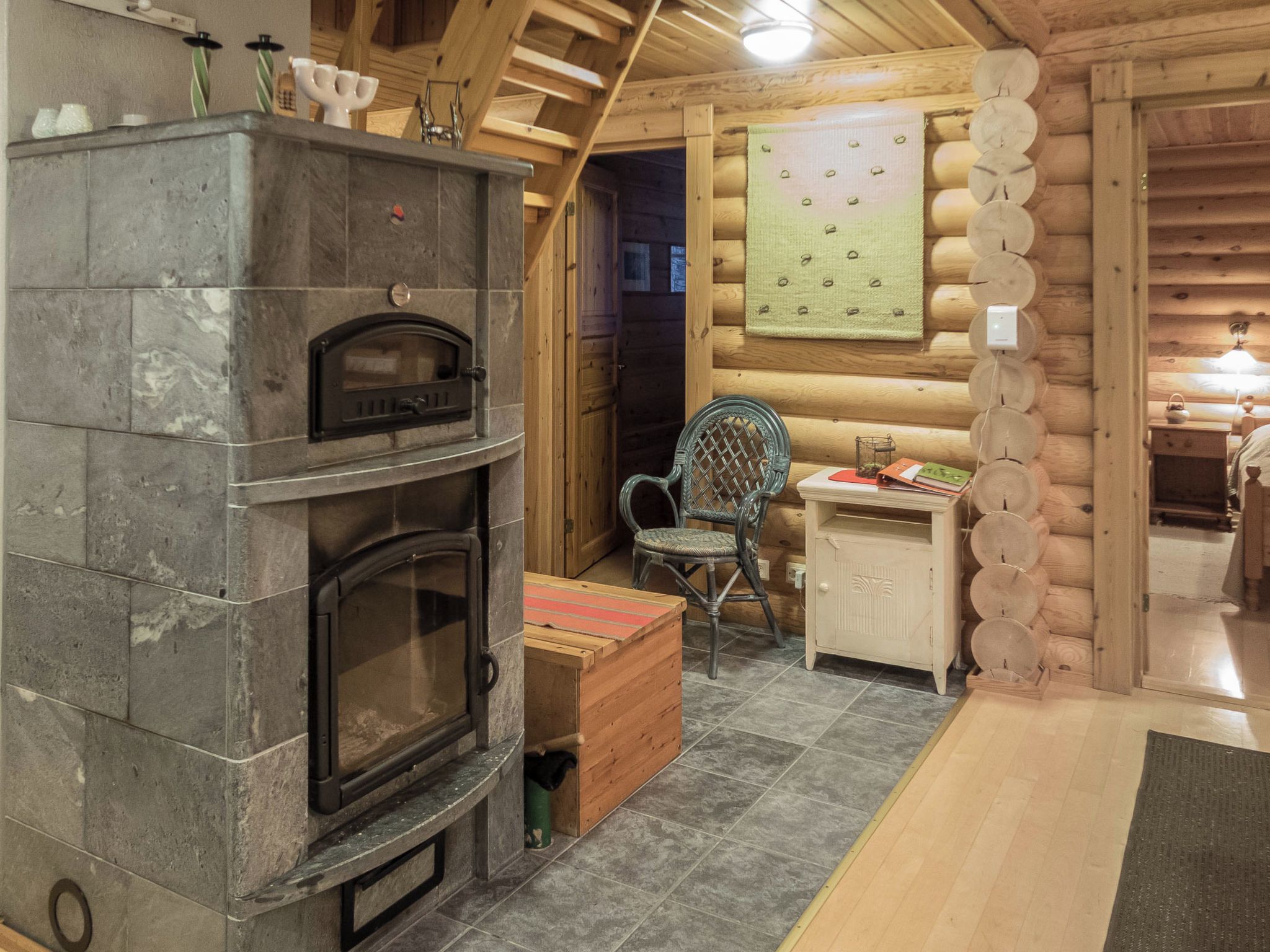 Interior de una cabaña de troncos con chimenea de piedra, una mesa de comedor de madera y una silla tejida.