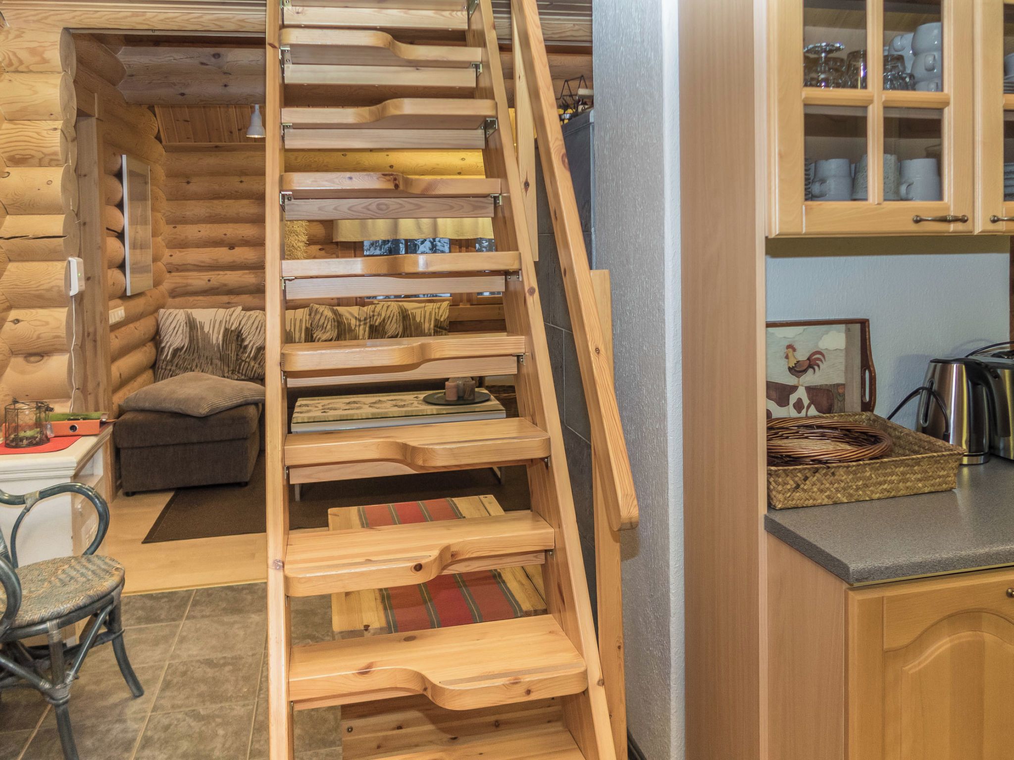 Una escalera de madera que lleva a un dormitorio en un entrepiso, con vista al área de la cocina.