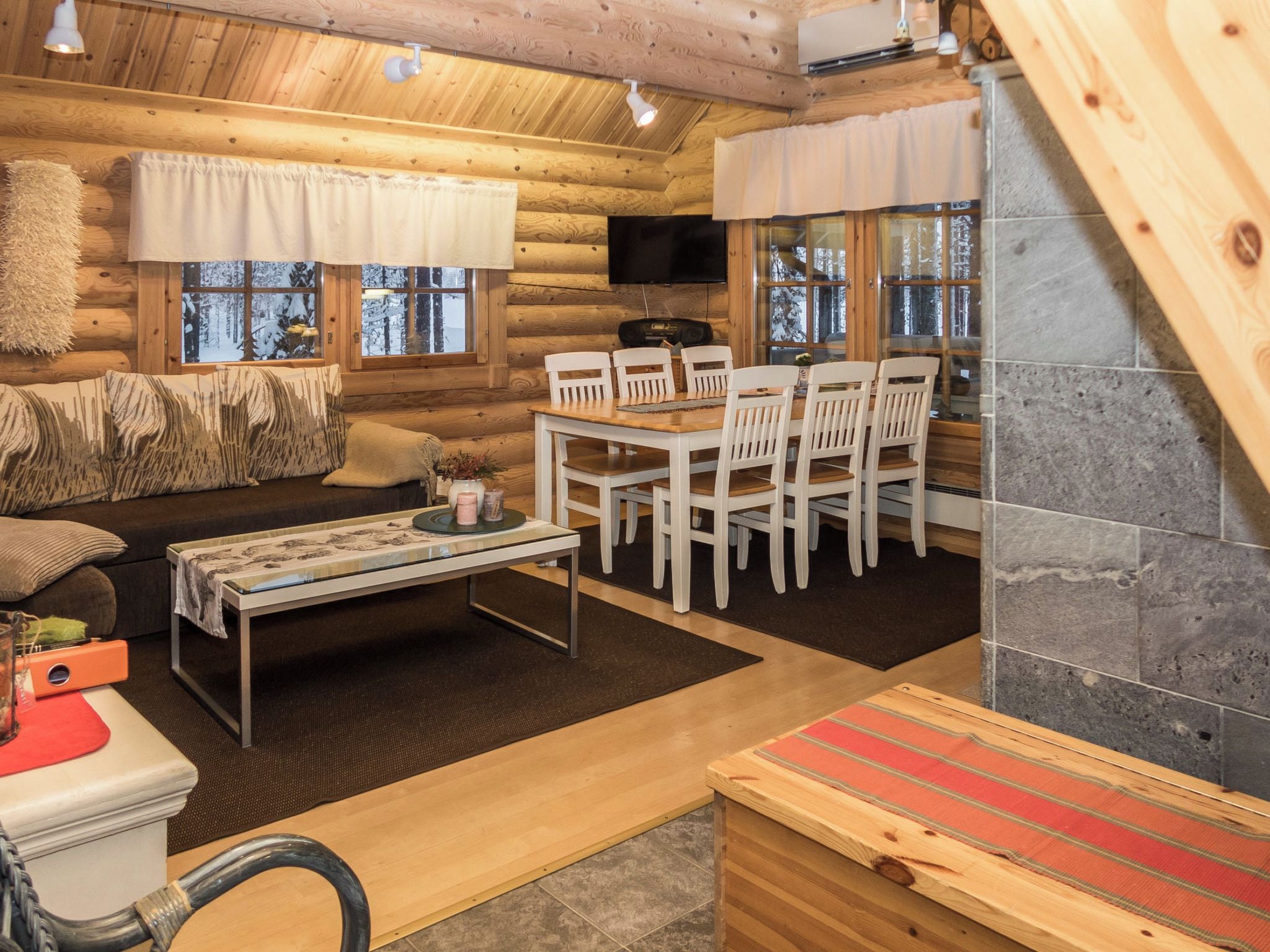 Acogedor interior de cabaña de madera con sofá, mesa de comedor, sillas y chimenea.