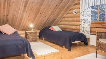 A cozy cabin with two beds, a small table, a lamp, and a window with a view of a snowy landscape.