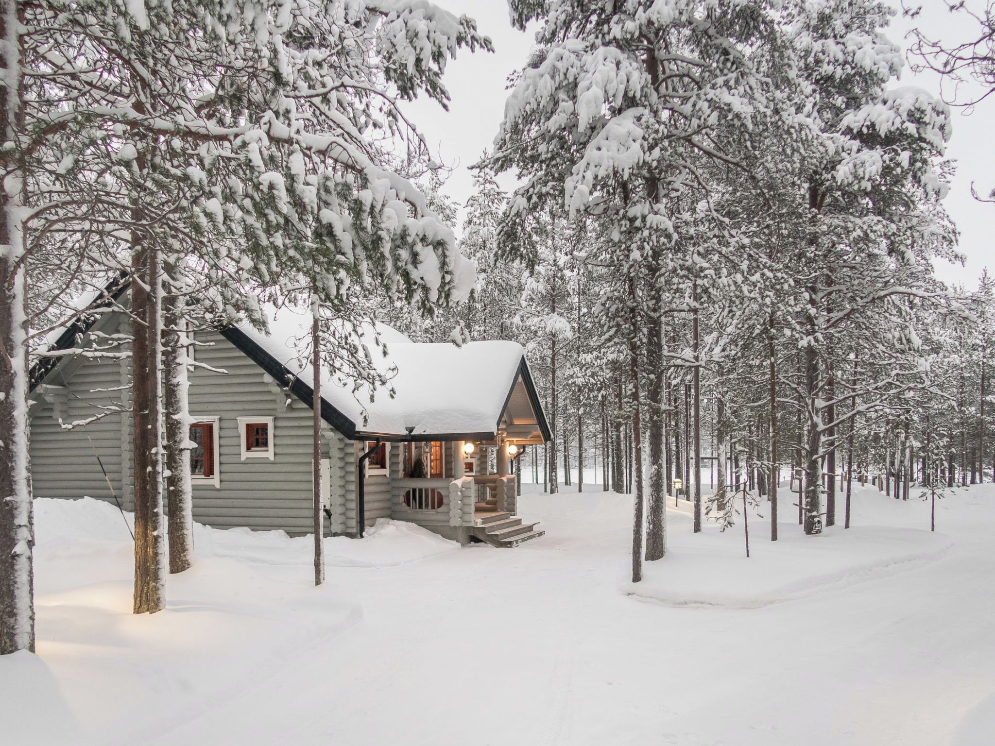 A log cabin with a porch, surrounded by snow-covered trees.