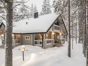 A log cabin with a snow-covered roof, surrounded by trees.