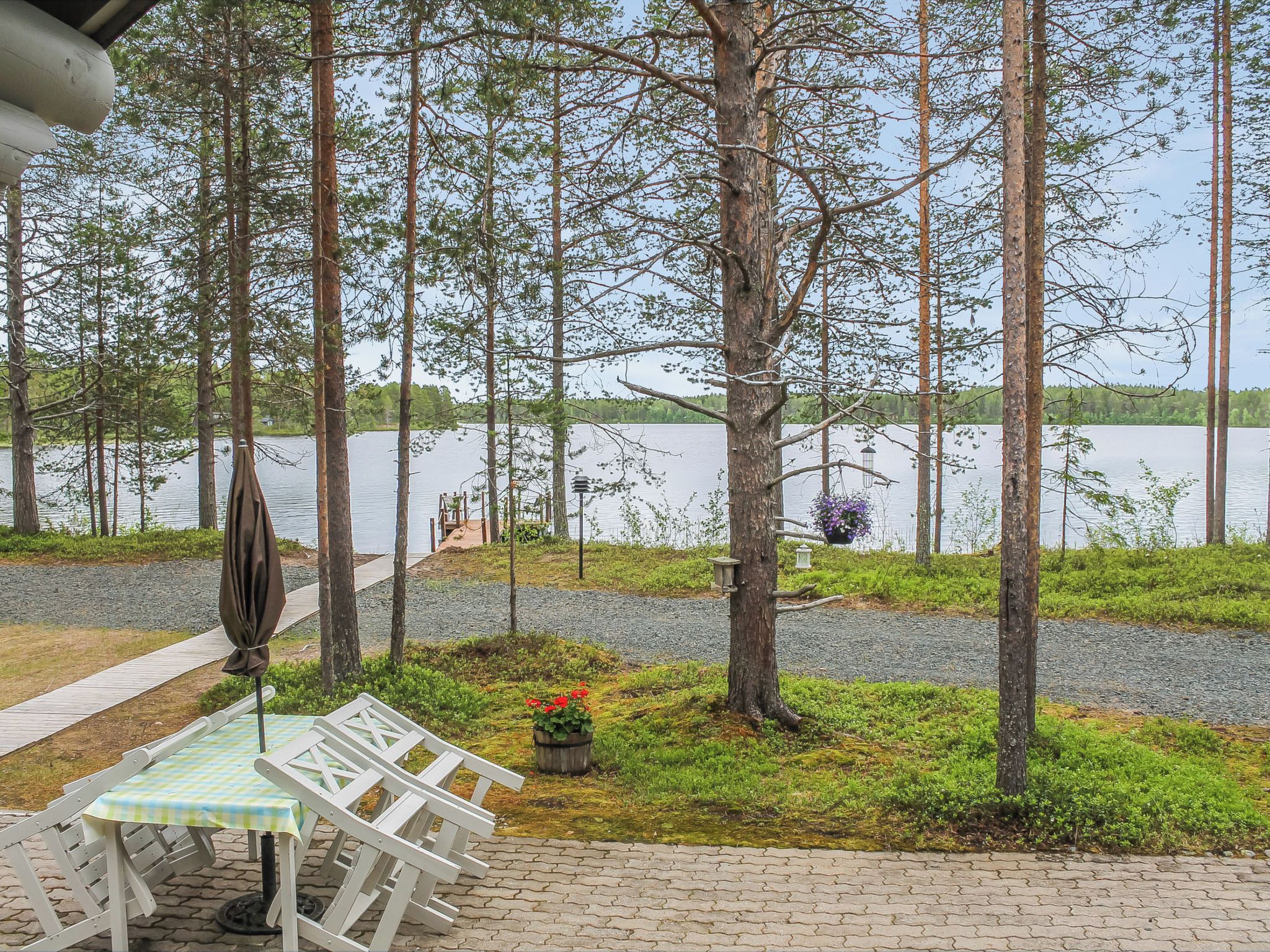 A lakeside patio with a table and chairs, surrounded by trees and a view of the lake.