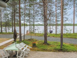 A lakeside patio with a table and chairs, surrounded by trees and a view of the lake. - Syväniemi by Interhome (Kuusamo)