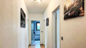 Un pasillo con piso de madera, paredes blancas y una puerta con ventana.