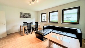 Una sala de estar moderna con un sofá de cuero negro, una mesa de comedor de vidrio con sillas, y un cuadro en la pared.