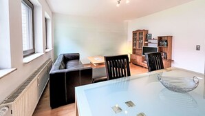 Una sala de estar moderna con una mesa de comedor de cristal, un sofá de cuero negro y un mueble de madera con puertas de vidrio.