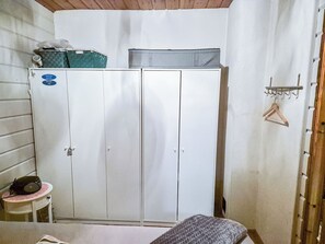 A room with a wardrobe, a small table with a radio, and a bed.