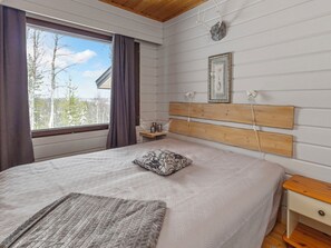 Un dormitorio con una cama grande, cabecera de madera, mesita de noche, cortinas en la ventana y un cuadro enmarcado en la pared.