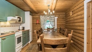 Interior de una cabaña de madera con cocina, mesa de comedor y sillas.