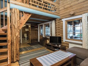 L’intérieur d’une cabane en rondins, avec un escalier, un téléviseur et une vue sur l’extérieur.