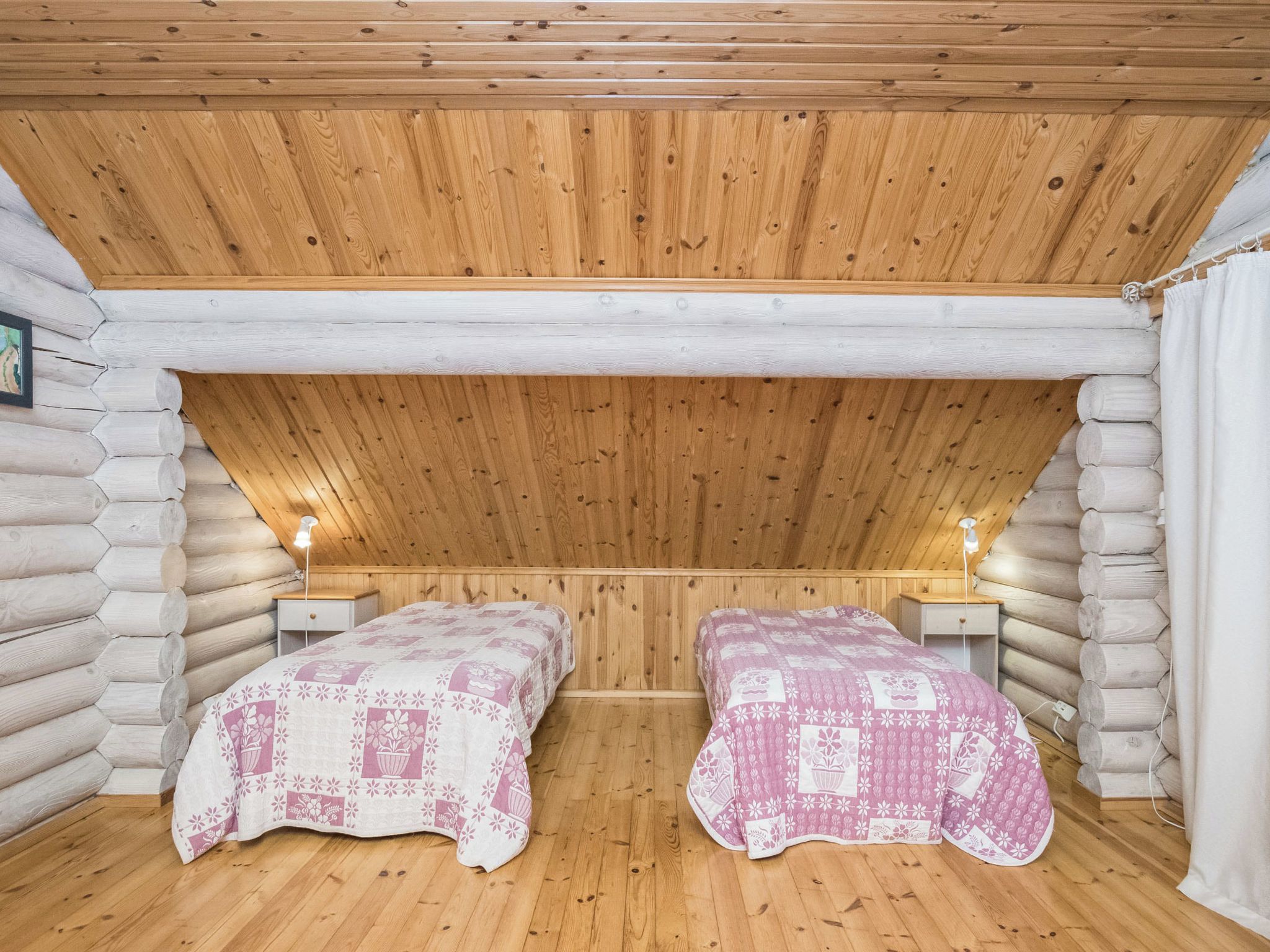 Een houten kamer in een blokhut met twee bedden, houten wanden en een schuine kap.