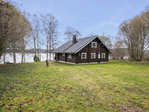 Une cabane en rondins avec un toit à pignon, une cheminée et un petit porche doté d’une seule fenêtre.