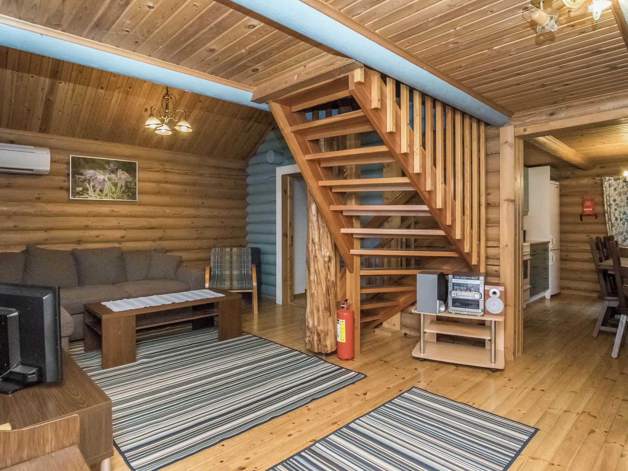 A log cabin interior with a wooden staircase, a sofa, a coffee table, a television, and a fireplace.