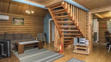 A log cabin interior with a wooden staircase, a sofa, a coffee table, a television, and a fireplace.