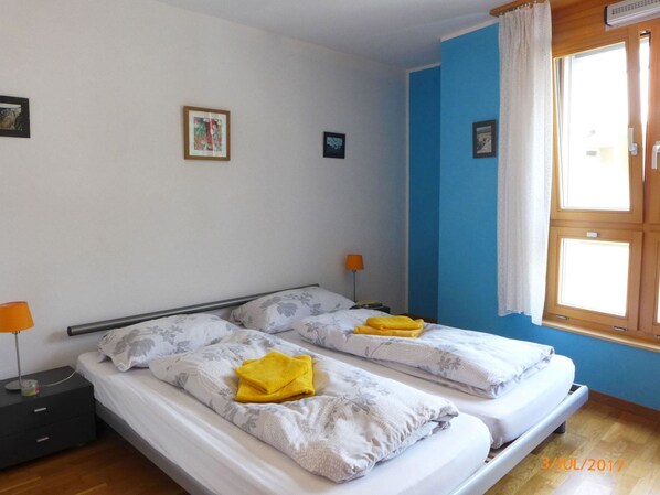 A room with two beds, a nightstand, a lamp, and a window with curtains.