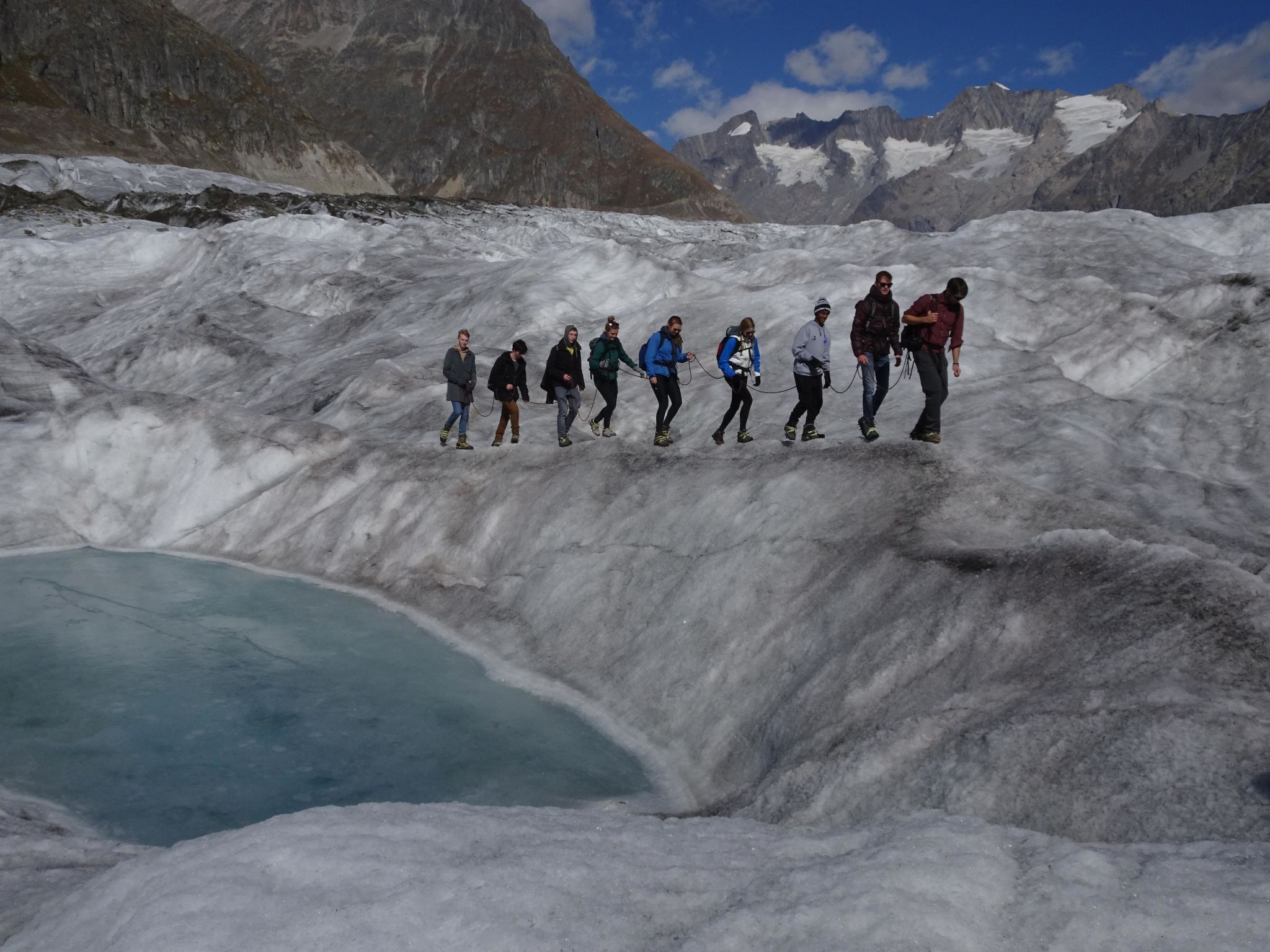 Un groupe de personnes marchant sur un glacier, avec des montagnes en arrière-plan.