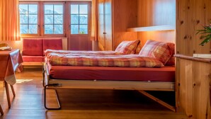 Un dormitorio acogedor con cama, escritorio y silla. Se ven montañas desde las ventanas.