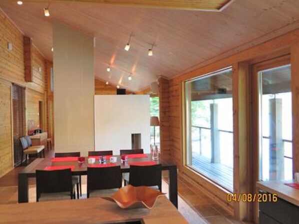 Un espace repas moderne avec une table et des chaises en bois, de grandes fenêtres et une vue sur l’extérieur.