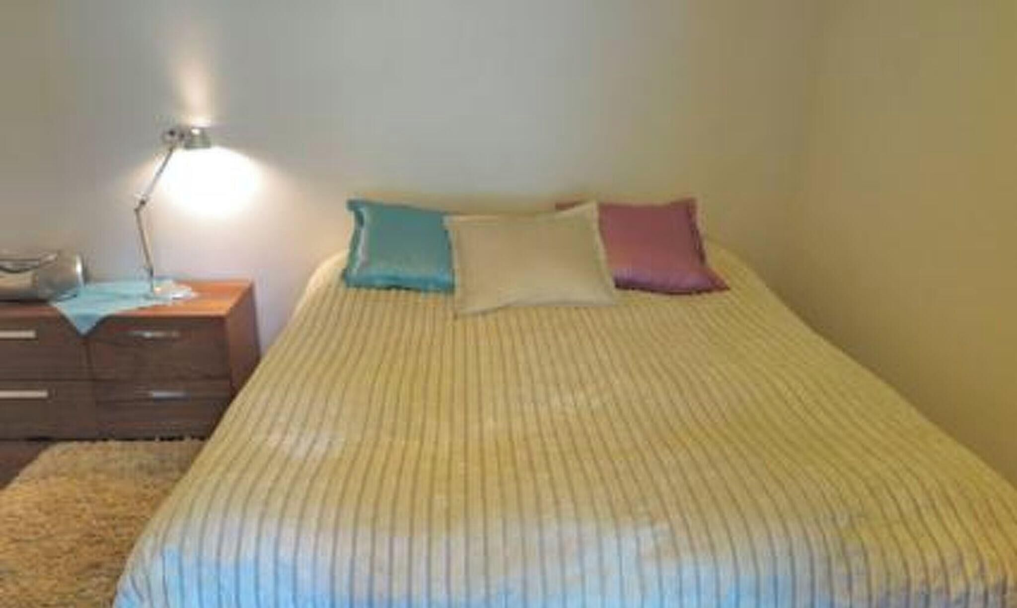 A simple, unadorned bedroom with a single bed, a bedside lamp, and a small wooden nightstand.