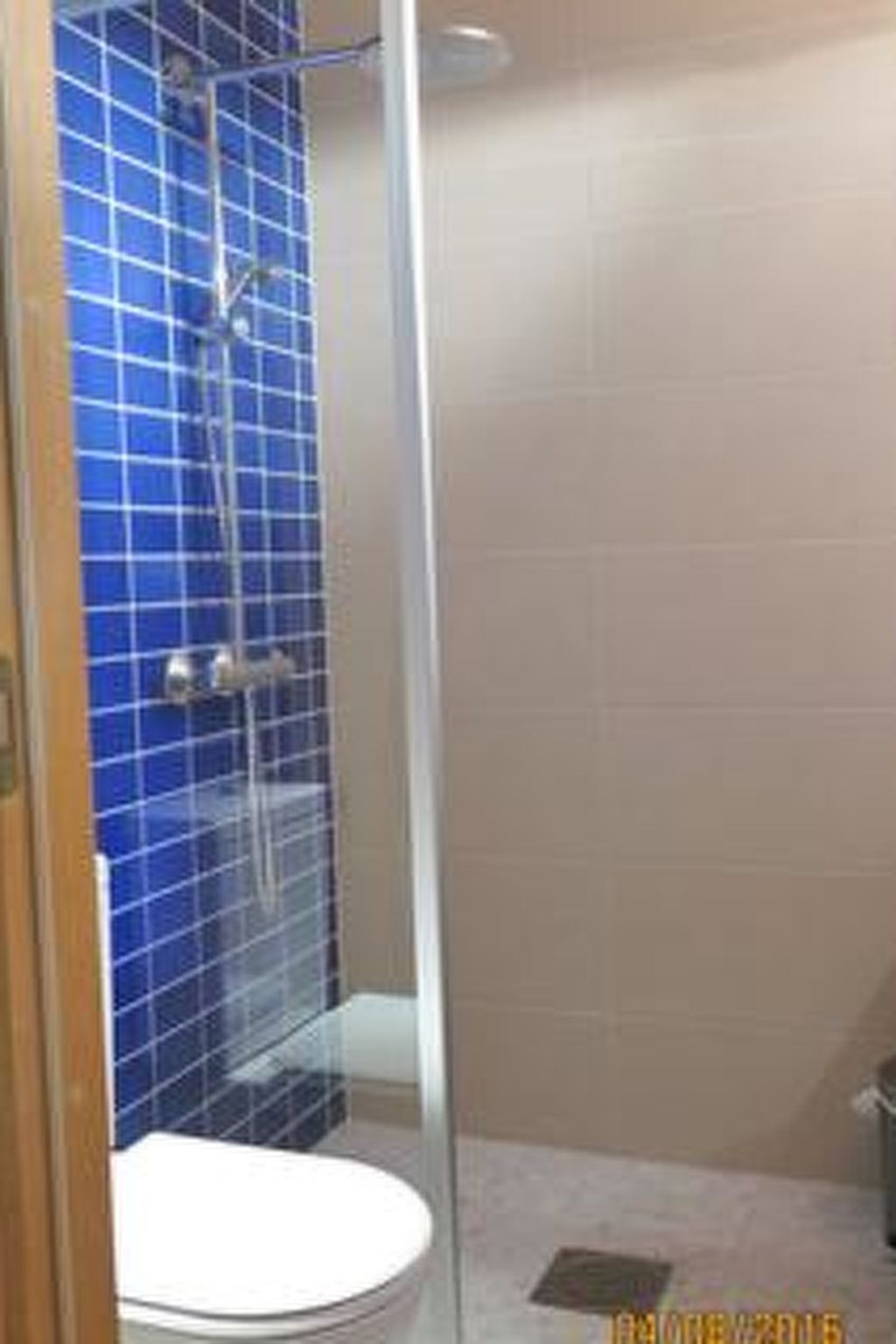Une salle de bain avec une douche à parois de verre, des toilettes blanches et des murs recouverts de carreaux bleus.