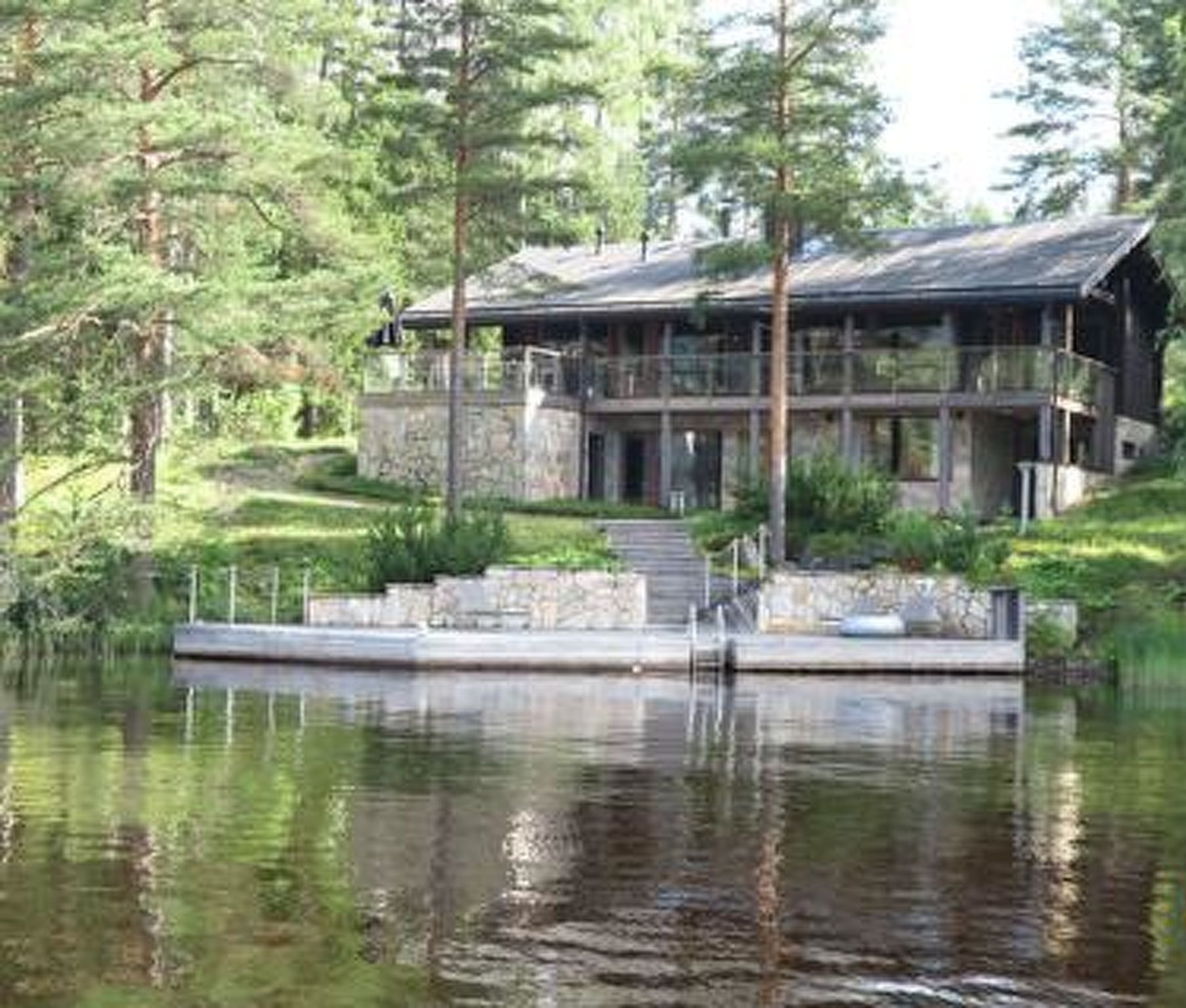 Un chalet au bord du lac, avec une façade en pierre, une terrasse et un escalier menant à l’entrée.