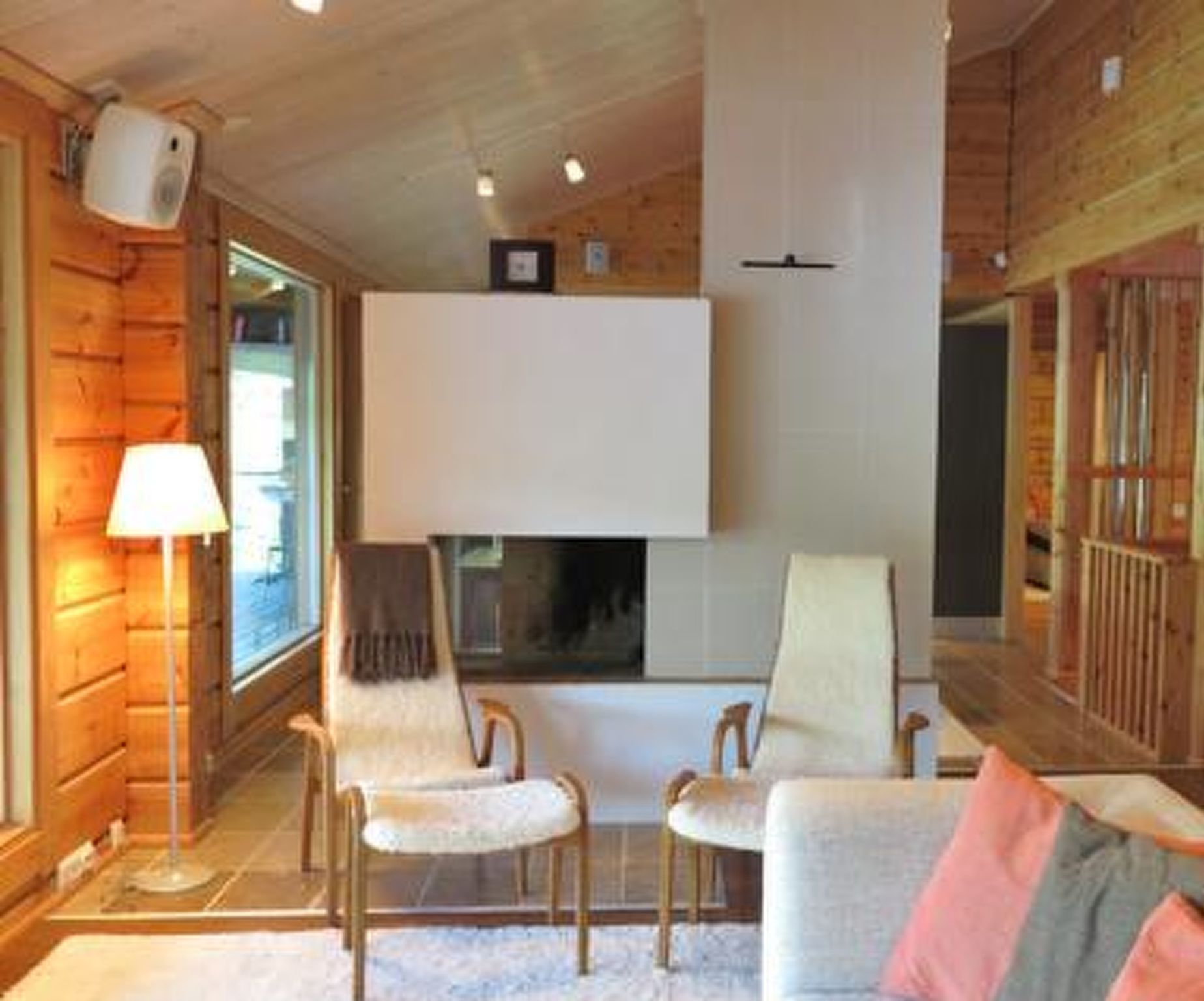 A cozy log cabin interior with a fireplace, two armchairs, a sofa, and a lamp.