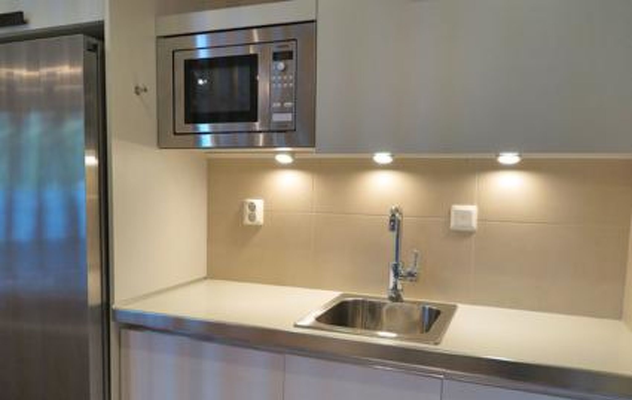 A modern kitchen with a stainless steel refrigerator, a built-in microwave, and a sink with under-cabinet lighting.