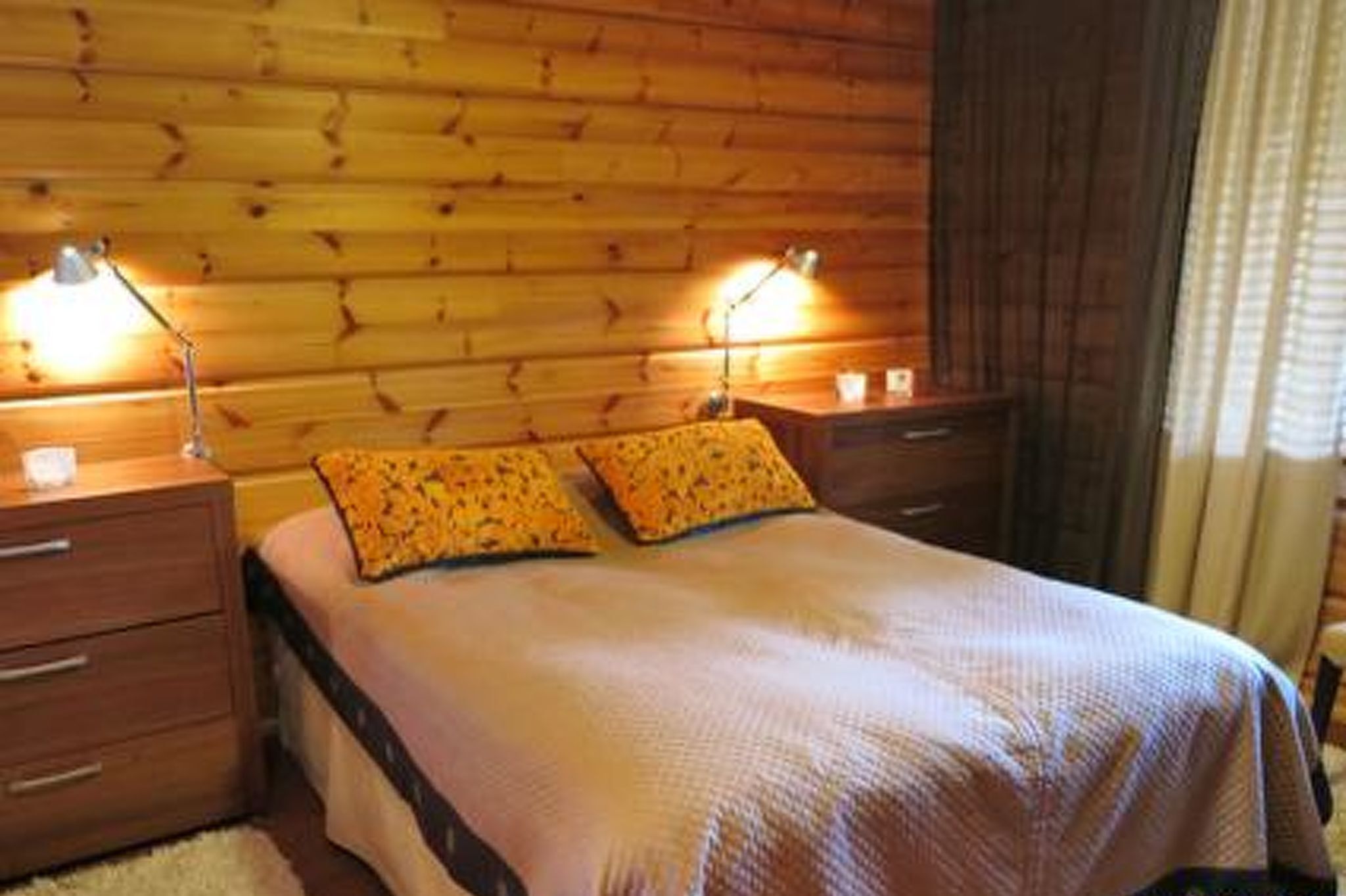 A wooden-paneled room with a bed, two bedside tables, and lamps.