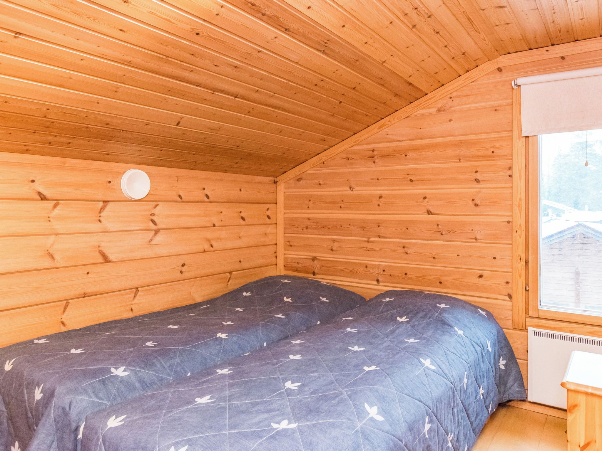 Una habitación pequeña de madera con cama, ventana y radiador.