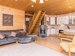 A cozy cabin interior with a wooden staircase, a fireplace, a kitchen, and a living area with a sofa and ottoman.