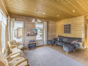 Una sala de estar acogedora con techo de madera, un sofá, un televisor y una chimenea.