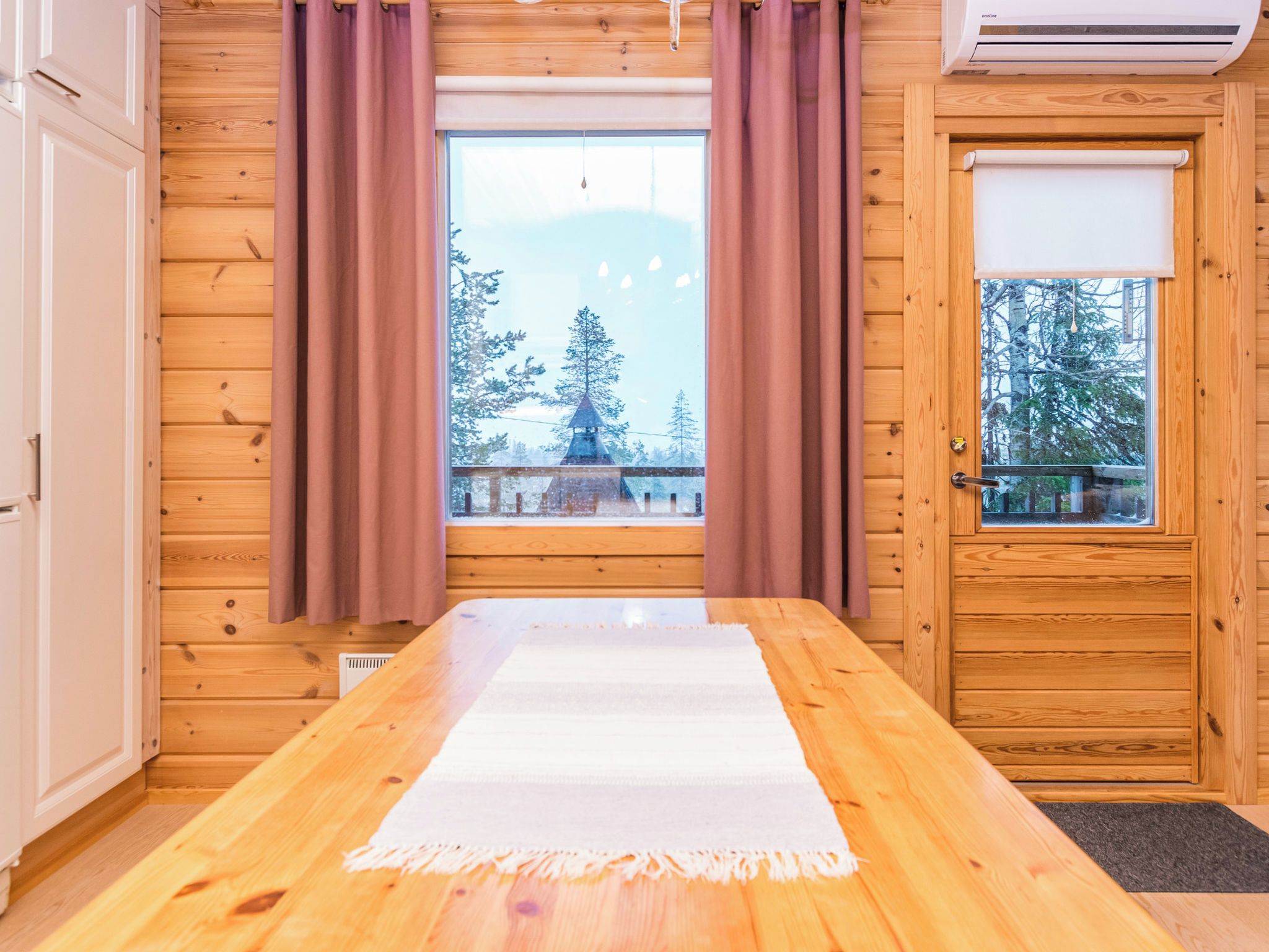 A room with wooden walls, a large window with curtains, a wooden table, and a door with a window.