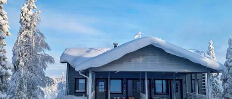 Een chalet bedekt met sneeuw, met een ruime veranda en een heldere lucht.