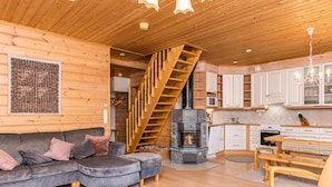 A cozy cabin interior with a wooden staircase, a sofa, a dining table, and a kitchen area.
