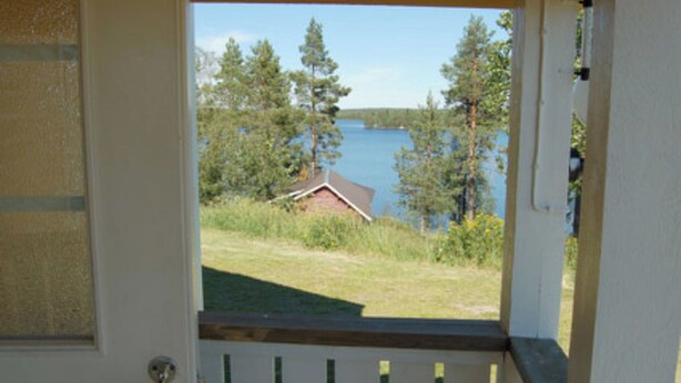 Une vue depuis une porte qui donne sur un espace verdoyant, avec un lac et des arbres en arrière-plan.