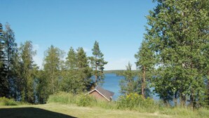 Une maison avec un toit en pente, entourée d’une pelouse et d’arbres, et qui offre une vue sur une étendue d’eau.
