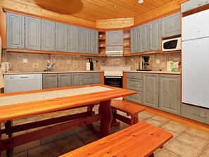Una cocina con armarios de madera, horno empotrado, microondas y una mesa de comedor de madera con bancos.