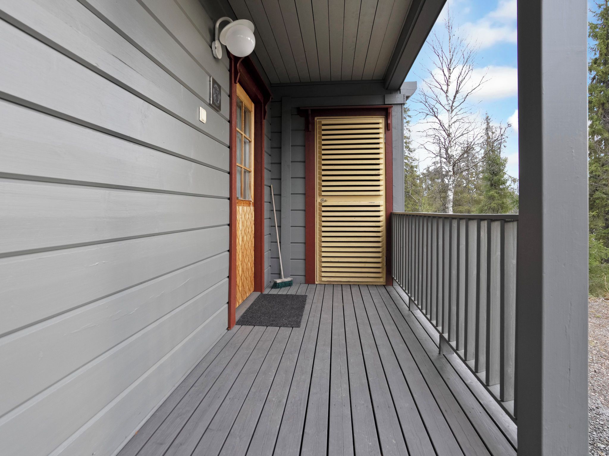 A wooden deck with a door and a window, a broom, and a doormat.