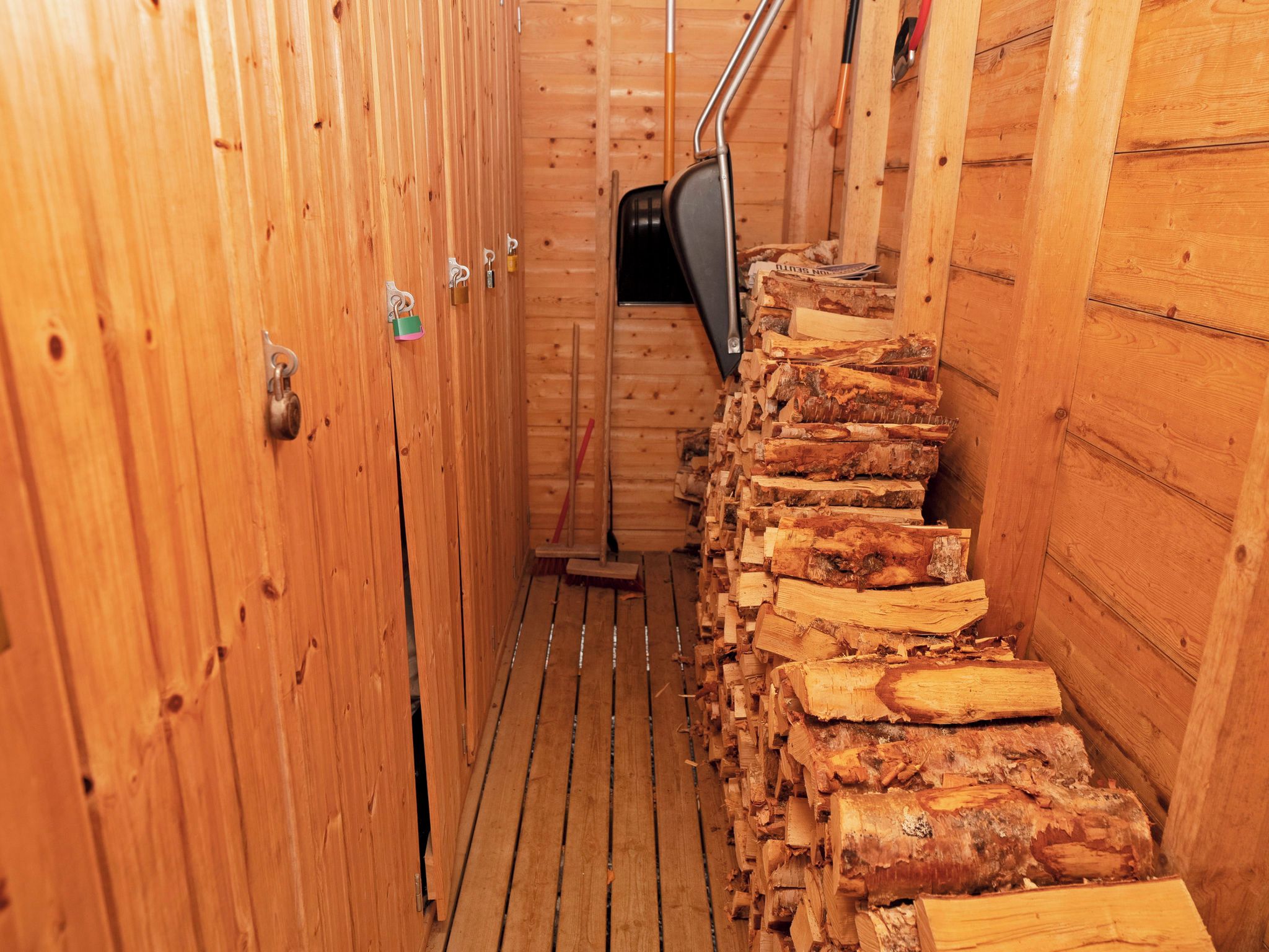 Un intérieur en bois, avec une pile de bois de chauffage, une échelle en métal et une porte fermée à clé.