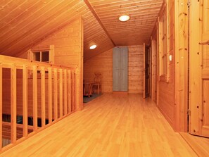 A wooden interior with a sloped ceiling, a staircase, and a door leading to another room.