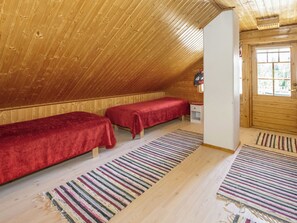 Une chambre mansardée chaleureuse, avec deux lits simples, un plafond en bois à pente et une fenêtre offrant une vue agréable.