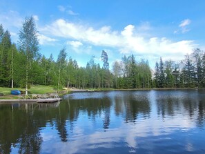 Ein ruhiger See mit einer Anlegestelle und einem Boot, umgeben von dichtem Wald.