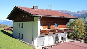 Una cabaña de dos pisos con un balcón, frente a un paisaje montañoso.