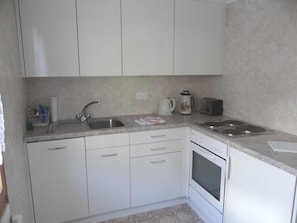 A kitchen with white cabinets, a stainless steel sink, a kettle, a toaster, and a dishwasher. - Valentine Appartement/Fewo 4-Bettwohnung by Interhome (Engelberg)