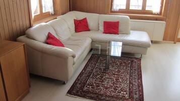 Ein Wohnzimmer mit Ecksofa in Beige, roten Kissen, einem Glastisch und einem gemusterten Teppich.