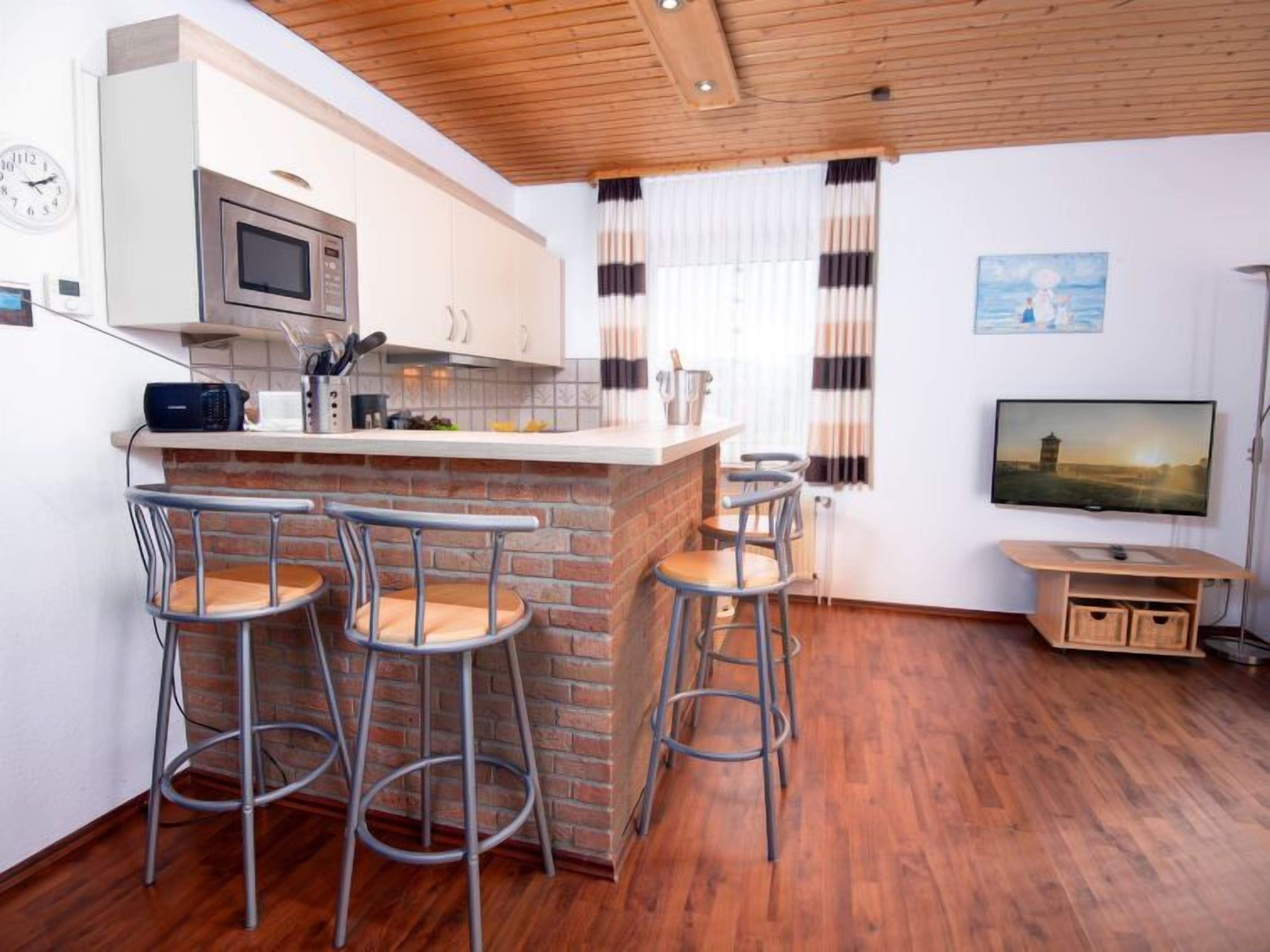 Una cocina moderna con una isla central, taburetes de bar, microondas y televisor.