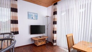 A modern living room with a flat-screen TV, wooden flooring, a dining table with chairs, and striped curtains. - Am Koper Sand by Interhome (Norddeich)